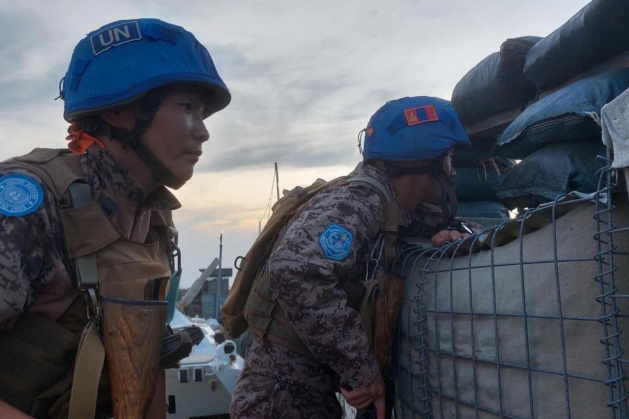 A close up photo of two Mongolian peacekeeper in their blue helmets and uniforms looking out from an outpost