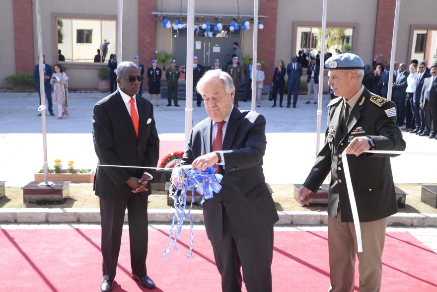 UN Secretary General Guterres cuts a ribbon during an outdoor inauguration ceremony, flanked by two uniformed officers.